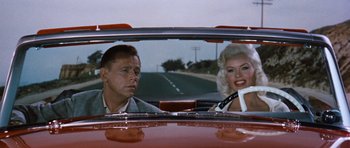 Movie still from “The Girl Can't Help It” (1956), directed by Frank Tashlin – A man and a woman sitting in the back seat of a red car; Medium shot, Over the shoulder angle