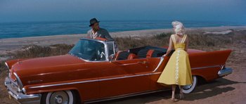 Movie still from “The Girl Can't Help It” (1956), directed by Frank Tashlin – A man and a woman standing next to an old red car; Wide shot, High angle