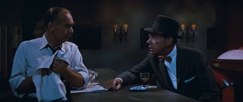 Movie still from “The Girl Can't Help It” (1956), directed by Frank Tashlin – Two men sitting at a table with a glass of wine; Medium shot, Over the shoulder angle