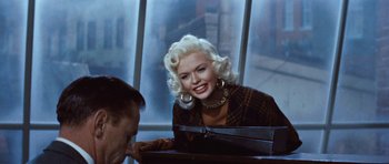 Movie still from “The Girl Can't Help It” (1956), directed by Frank Tashlin – A woman with blonde curly hair and a large smile on her face; Medium shot, Over the shoulder angle