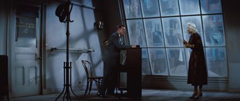 Movie still from “The Girl Can't Help It” (1956), directed by Frank Tashlin – A man standing at a podium in front of a large window; Wide shot, Low angle