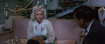 Movie still from “The Girl Can't Help It” (1956), directed by Frank Tashlin – A woman sitting on top of a couch wearing a white shirt; Medium shot, Over the shoulder angle