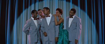 Movie still from “The Girl Can't Help It” (1956), directed by Frank Tashlin – A group of men and a woman standing next to each other in front of a curtain; Medium shot, Low angle