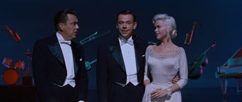 Movie still from “The Girl Can't Help It” (1956), directed by Frank Tashlin – A man and two women in tuxedos standing next to each other; Medium shot, Low angle