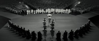 Movie still from “The Giver” (2014), directed by Phillip Noyce – A black and white photo of a group of people standing in front of an audience; Extreme Wide shot, High angle