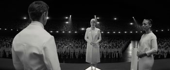 Movie still from “The Giver” (2014), directed by Phillip Noyce – A black and white photo of a woman standing in front of an audience; Wide shot, Over the shoulder angle