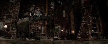Movie still from “The Giver” (2014), directed by Phillip Noyce – Two people sitting on a platform in a library; Wide shot, High angle
