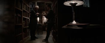 Movie still from “The Giver” (2014), directed by Phillip Noyce – Two people standing in a dark room looking at a book; Wide shot, Over the shoulder angle