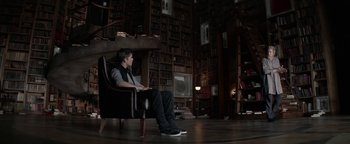 Movie still from “The Giver” (2014), directed by Phillip Noyce – A man sitting in a chair in a room filled with books; Wide shot, Over the shoulder angle
