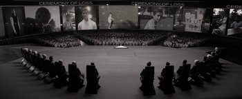 Movie still from “The Giver” (2014), directed by Phillip Noyce – A crowd of people sitting in chairs in front of a large screen; Wide shot, High angle