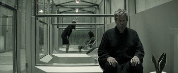 Movie still from “The Giver” (2014), directed by Phillip Noyce – A man sitting on a chair in a room with two women; Wide shot, High angle