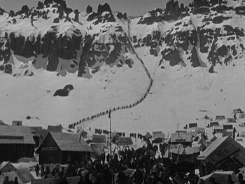Movie still from “The Gold Rush” (1925), directed by Charles Chaplin – A crowd of people standing on top of a snow covered slope; Extreme Wide shot, High angle
