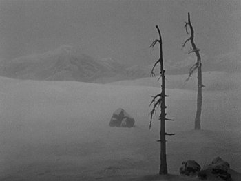 Movie still from “The Gold Rush” (1925), directed by Charles Chaplin – A black and white photo of trees in the snow; Extreme Wide shot, High angle