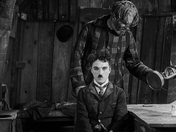 Movie still from “The Gold Rush” (1925), directed by Charles Chaplin – A man and a boy dressed up as charlie chaplin; Medium shot, High angle
