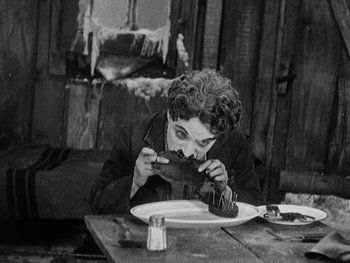 Movie still from “The Gold Rush” (1925), directed by Charles Chaplin – An old photo of a woman eating a piece of cake; Medium shot, High angle