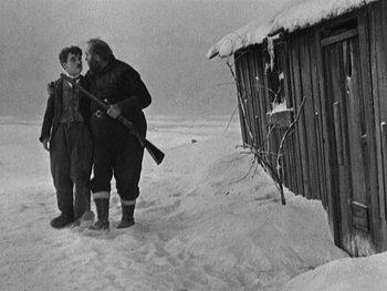 Movie still from “The Gold Rush” (1925), directed by Charles Chaplin – A man and a boy standing in the snow with a gun; Wide shot, Low angle