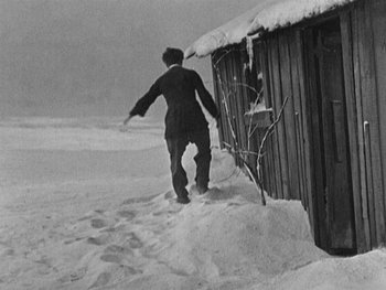 Movie still from “The Gold Rush” (1925), directed by Charles Chaplin – A man walking on the snow near a building; Wide shot, Low angle