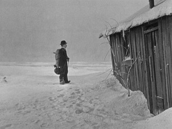 Movie still from “The Gold Rush” (1925), directed by Charles Chaplin – A man standing in the middle of a snow covered field; Wide shot, High angle