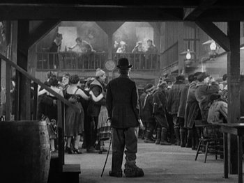 Movie still from “The Gold Rush” (1925), directed by Charles Chaplin – An old photo of a man standing in front of a crowd; Wide shot, Low angle