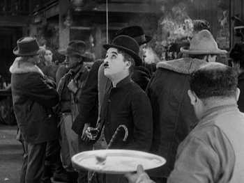 Movie still from “The Gold Rush” (1925), directed by Charles Chaplin – A man with a mustache wearing a top hat and holding a tray; Medium shot, High angle