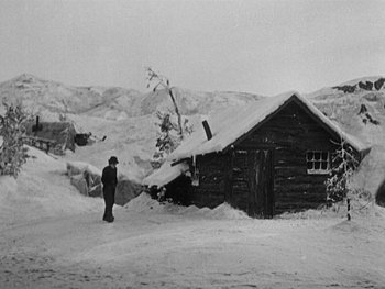 Movie still from “The Gold Rush” (1925), directed by Charles Chaplin – A person standing in front of a house in the snow; Extreme Wide shot, High angle