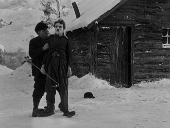 Movie still from “The Gold Rush” (1925), directed by Charles Chaplin – A man and a woman standing next to each other in the snow; Wide shot, Over the shoulder angle