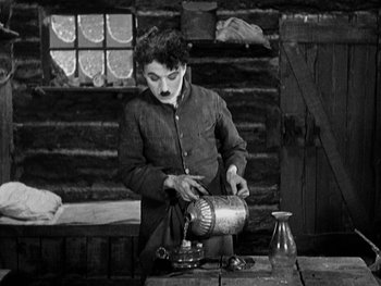 Movie still from “The Gold Rush” (1925), directed by Charles Chaplin – An old photo of a man making a drink; Medium shot, High angle