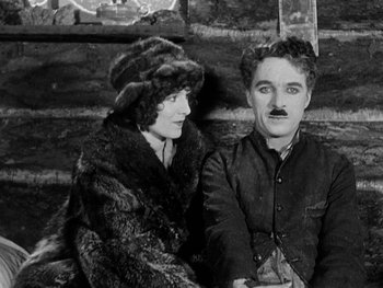 Movie still from “The Gold Rush” (1925), directed by Charles Chaplin – An old photo of a man and a woman sitting next to each other; Medium shot, High angle