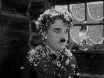 Movie still from “The Gold Rush” (1925), directed by Charles Chaplin – An old photo of a man with a beard and mustache covered in powdery substance; Close Up shot, High angle