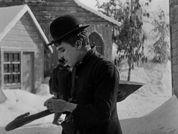 Movie still from “The Gold Rush” (1925), directed by Charles Chaplin – A man wearing a hat and holding a cell phone in his hand; Medium shot, Low angle