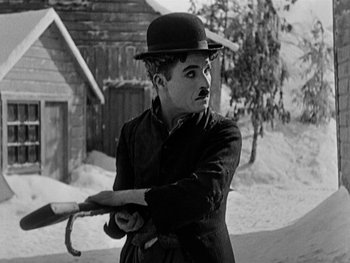 Movie still from “The Gold Rush” (1925), directed by Charles Chaplin – A black and white photo of a man holding a baseball bat; Medium shot, Low angle