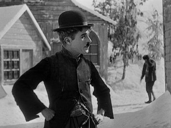 Movie still from “The Gold Rush” (1925), directed by Charles Chaplin – An old photo of a man with a hat and a mustache; Medium shot, Low angle