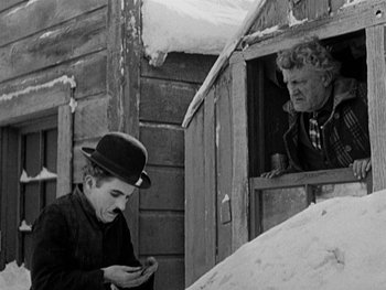 Movie still from “The Gold Rush” (1925), directed by Charles Chaplin – An old black and white photo of a man looking at a cell phone; Medium shot, Low angle