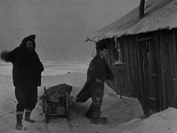 Movie still from “The Gold Rush” (1925), directed by Charles Chaplin – A man and a woman pulling a sled down a snow covered slope; Wide shot, High angle