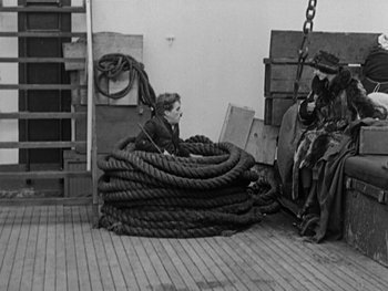 Movie still from “The Gold Rush” (1925), directed by Charles Chaplin – A boy sitting on a pile of ropes on a boat; Wide shot, High angle