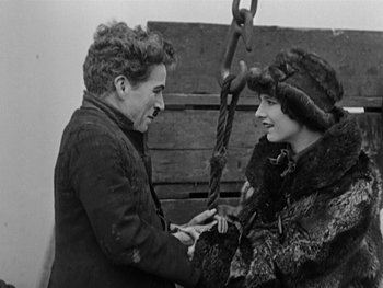 Movie still from “The Gold Rush” (1925), directed by Charles Chaplin – A man and a woman are holding hands and smiling at each other; Medium shot, High angle
