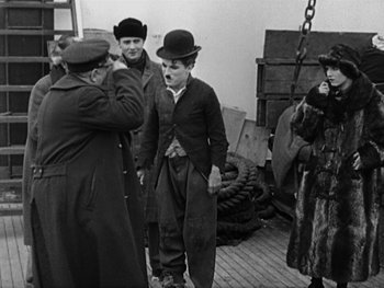 Movie still from “The Gold Rush” (1925), directed by Charles Chaplin – A group of men standing on top of a wooden deck; Medium shot, Over the shoulder angle