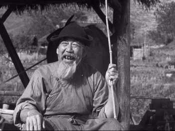 Movie still from “The Good Earth” (1937), directed by Sidney Franklin – An old man sitting in a chair holding a stick; Medium shot, Low angle