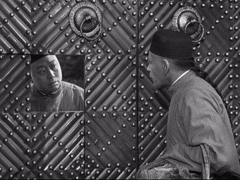 Movie still from “The Good Earth” (1937), directed by Sidney Franklin – An old man sitting in front of a metal wall; Medium shot, Over the shoulder angle