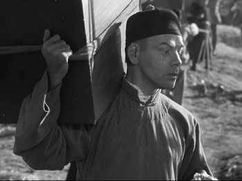 Movie still from “The Good Earth” (1937), directed by Sidney Franklin – A man holding an umbrella while standing on a dirt road; Medium shot, Low angle