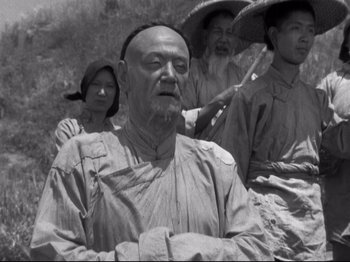 Movie still from “The Good Earth” (1937), directed by Sidney Franklin – An old man with a beard and a hat is in front of a group of people; Medium shot, Low angle