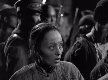 Movie still from “The Good Earth” (1937), directed by Sidney Franklin – A black and white photo of a woman in front of a group of soldiers; Close Up shot, Over the shoulder angle