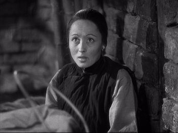 Movie still from “The Good Earth” (1937), directed by Sidney Franklin – A black and white photo of a woman sitting against a brick wall; Close Up shot, High angle