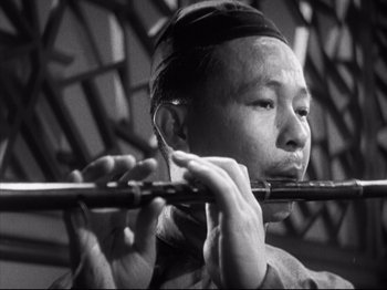 Movie still from “The Good Earth” (1937), directed by Sidney Franklin – An asian man playing a flute in front of a mirror; Close Up shot, Low angle