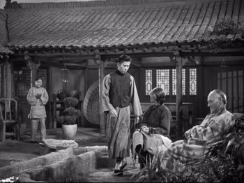 Movie still from “The Good Earth” (1937), directed by Sidney Franklin – An old black and white photo of a man standing in front of other men; Wide shot, High angle