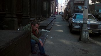 Movie still from “The Goodbye Girl” (1977), directed by Herbert Ross – A man sitting on the side of the street next to a building; Wide shot, High angle