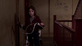Movie still from “The Goodbye Girl” (1977), directed by Herbert Ross – A young girl standing next to a bicycle in a building; Medium shot, Low angle