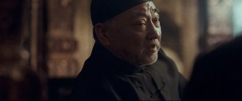 Movie still from “The Grandmaster” (2013), directed by Kar-Wai Wong – An older man wearing a black hat and a black robe; Close Up shot, Over the shoulder angle