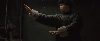 Movie still from “The Grandmaster” (2013), directed by Kar-Wai Wong – A man in a black jacket is holding something up; Medium shot, Low angle