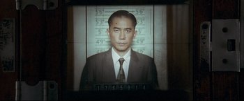 Movie still from “The Grandmaster” (2013), directed by Kar-Wai Wong – A man in a suit and tie in front of a mugshot; Close Up shot, Low angle